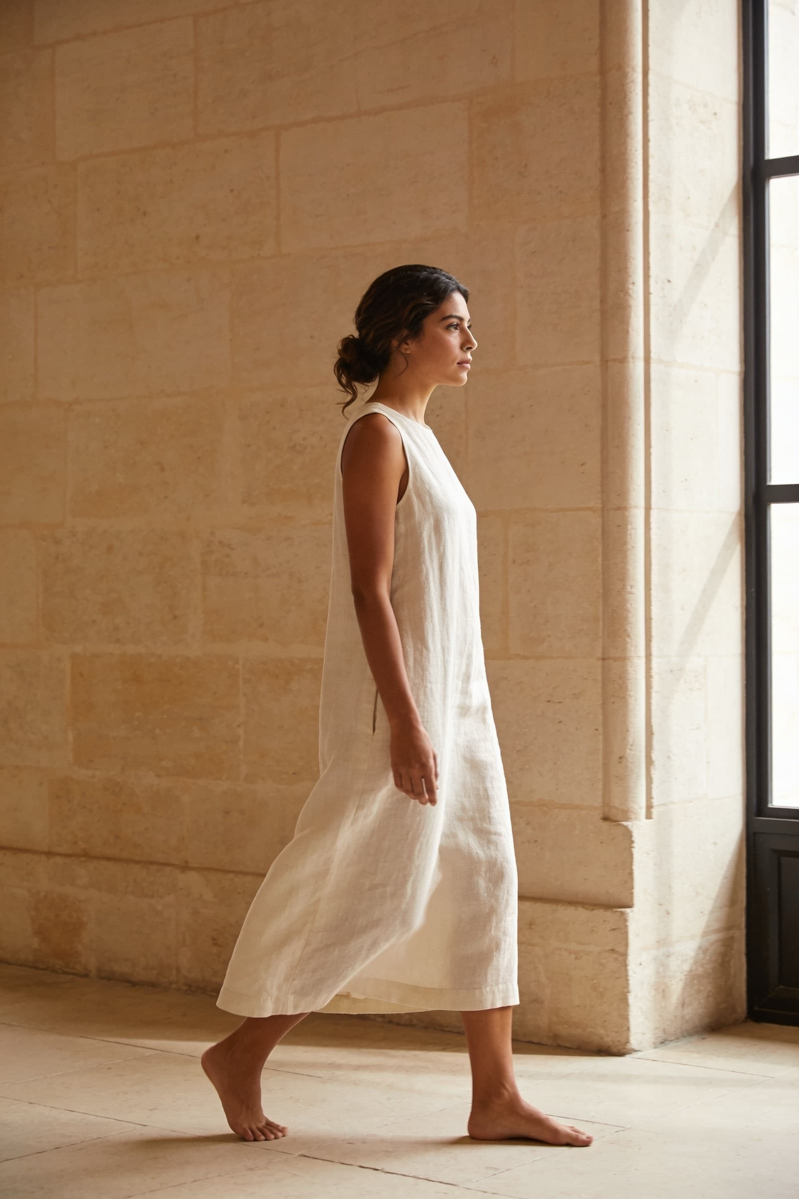 Mujer con vestido de lino ivory caminando junto a un muro de cantera