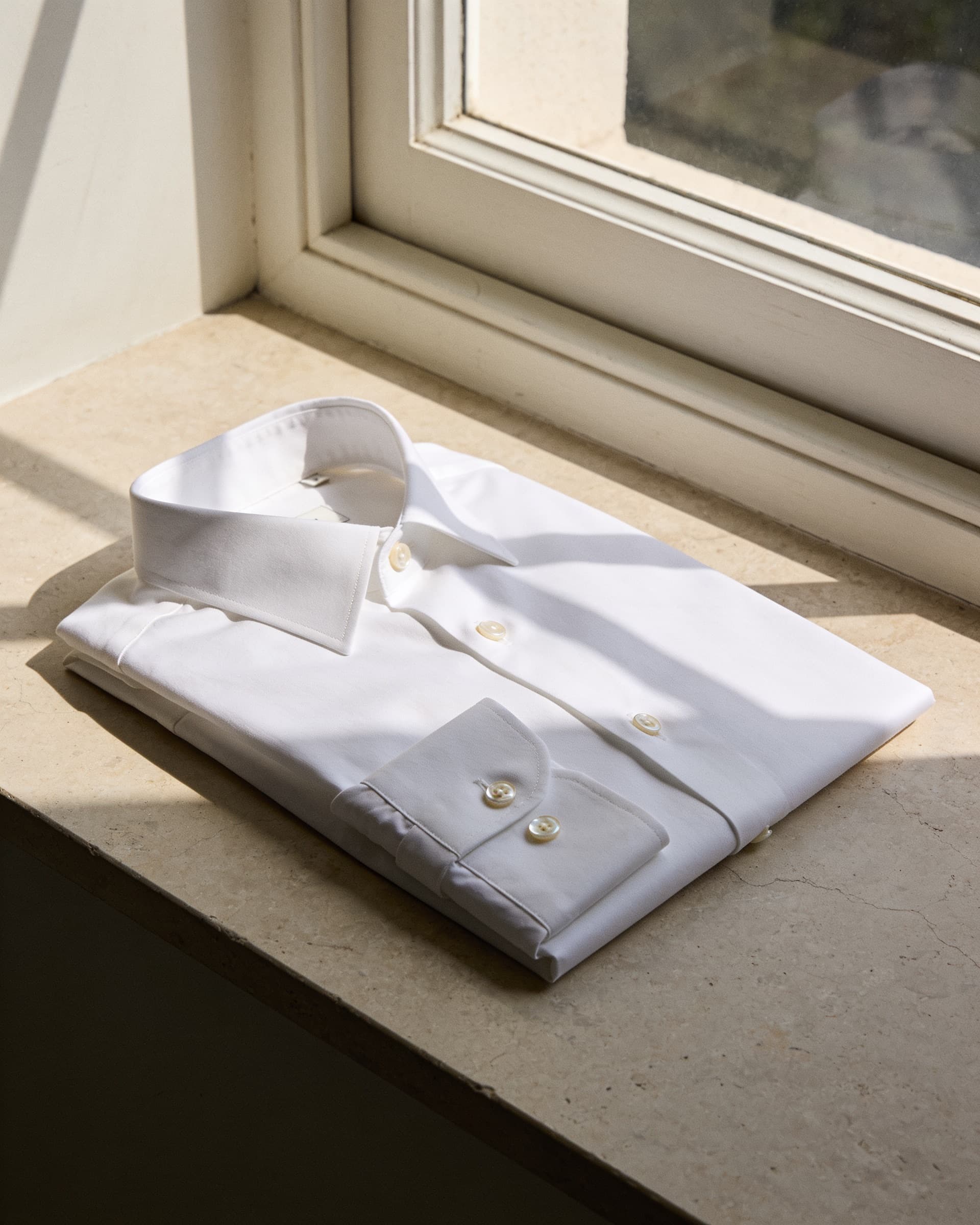 Cuello y botones de nácar de la camisa de popelina ivory, doblada sobre piedra